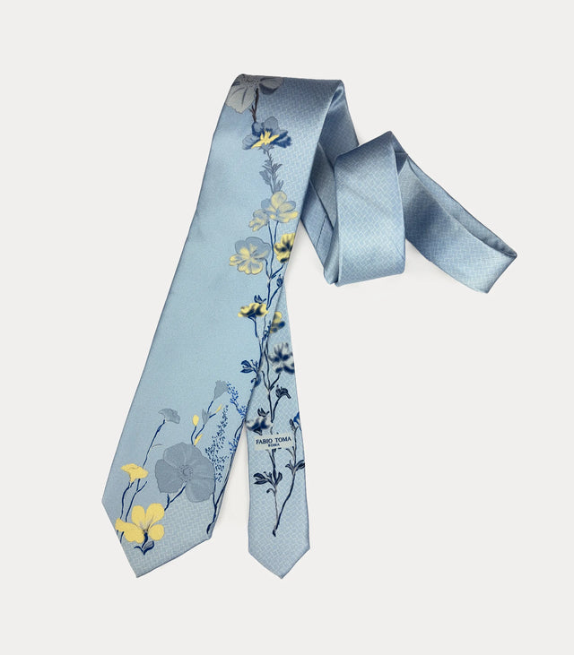 Cravatta celeste con fiori gialli e grigi, codino floreale coordinato e logo Fabio Toma Roma stampato.