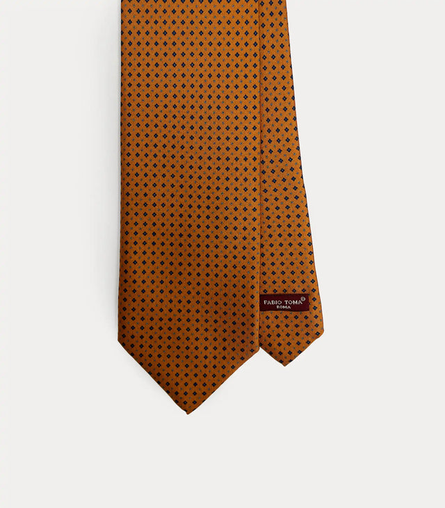 Dettaglio frontale cravatta Fabio Toma Roma in seta arancione ruggine con micro pattern geometrico blu, etichetta visibile.