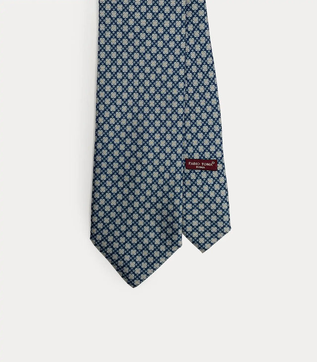 Dettaglio ravvicinato della cravatta Fabio Toma Roma in seta blu con micro pattern floreale bianco e celeste, vista frontale con etichetta.