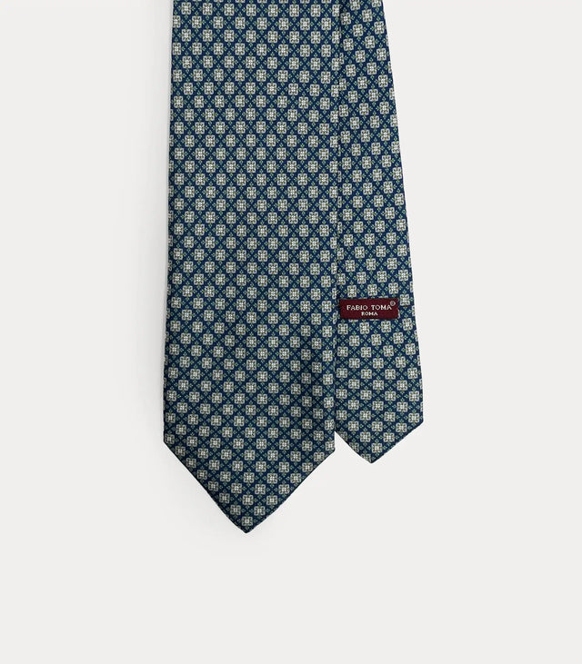 Dettaglio ravvicinato della cravatta Fabio Toma Roma in seta blu con micro pattern floreale bianco e verde, vista frontale con etichetta.