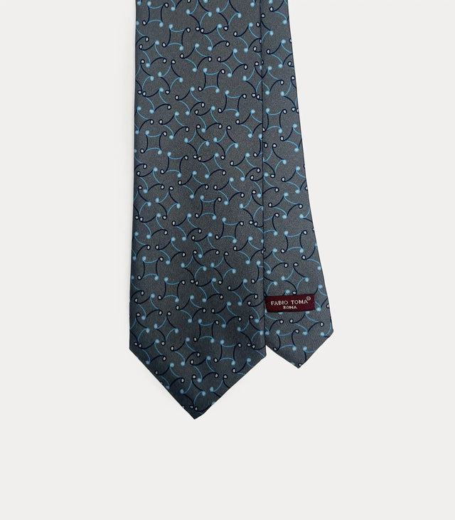 Dettaglio frontale della cravatta Fabio Toma Roma in seta grigio antracite con pattern fluido a volute azzurre e bianche, etichetta visibile.