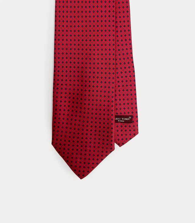 Dettaglio frontale cravatta Fabio Toma Roma in seta rossa con micro pattern geometrico blu, etichetta del brand visibile.