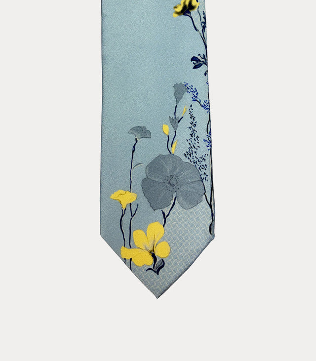 Cravatta Fabio Toma in seta celeste con fiori gialli e grigi e steli blu scuro lungo il lato e sulla punta.