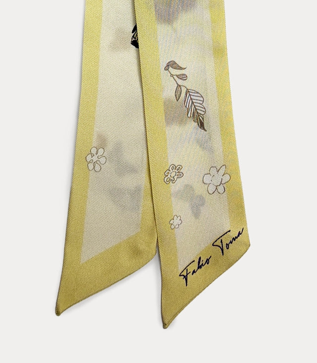 Dettaglio ravvicinato della stampa primaverile sul foulard twilly, che mette in risalto il contrasto tra il bordo giallo pastello, il disegno della farfalla, i contorni dei fiori bianchi e la raffinata trama del tessuto.