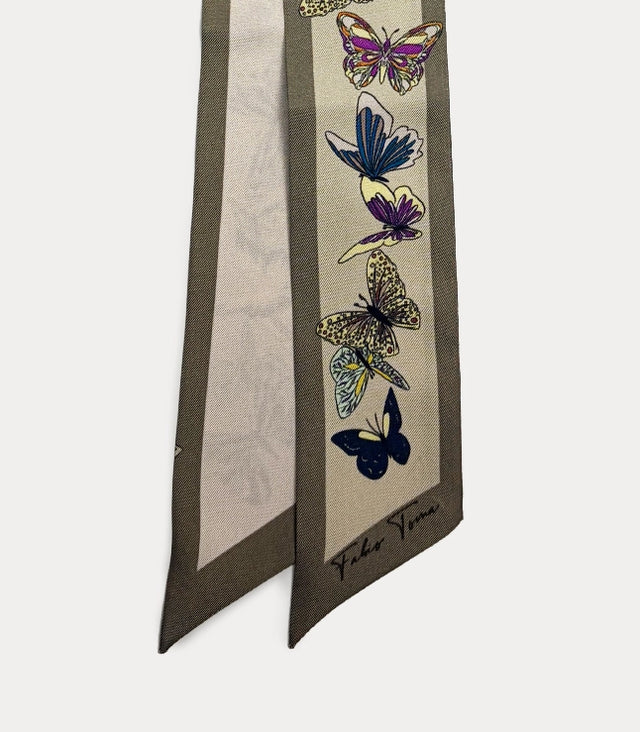 Dettaglio ravvicinato della stampa a farfalle sul foulard, che mette in risalto i colori vivaci delle ali in blu e viola, i dettagli del disegno e la trama del tessuto leggero.