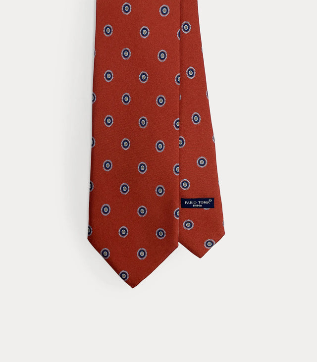 Cravatta rosso ruggine in pura seta con motivo circolare azzurro fatta a mano in Italia.