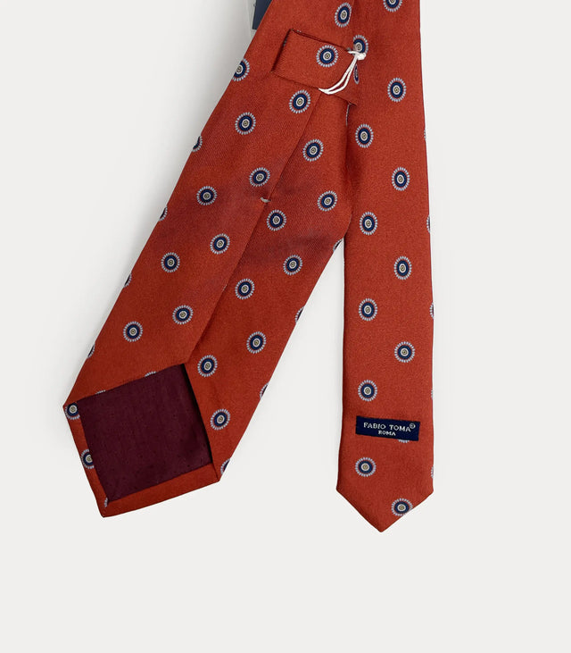 Cravatta rosso ruggine in pura seta con motivo circolare azzurro fatta a mano in Italia.